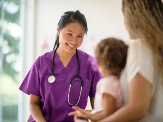 A caring nurse in purple scrubs having a conversation with a young patient